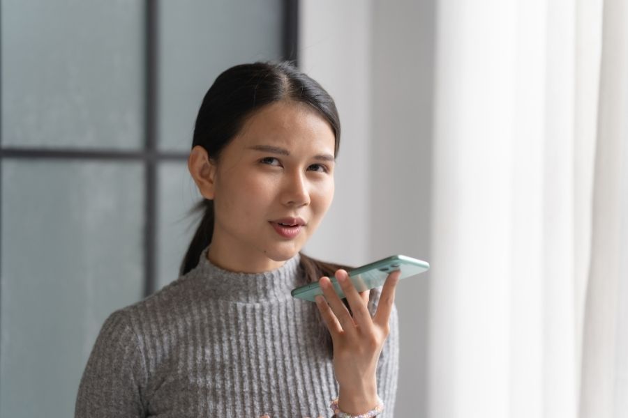 A woman speaking into her smartphone to use AI voice generators.